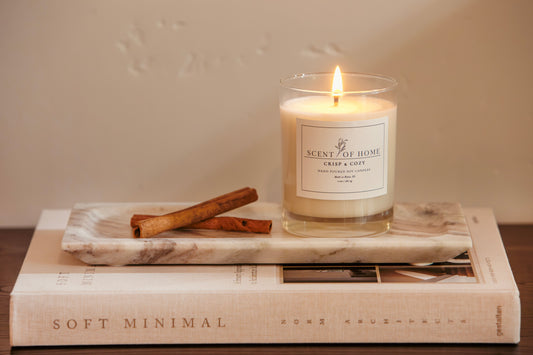 Scent of Home Crisp & Cozy soy candle burning on a marble tray with cinnamon sticks, styled on a design book for a soft, minimalist fall look.