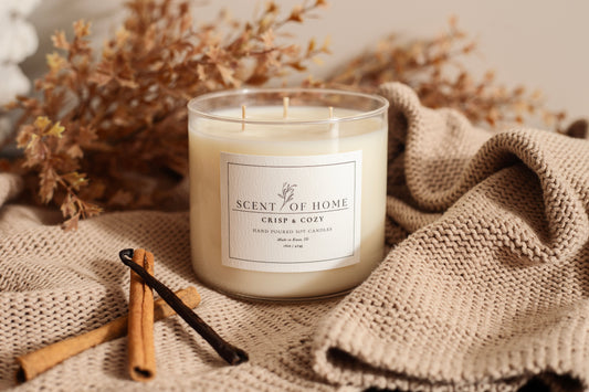 Scent of Home Crisp & Cozy soy candle surrounded by cinnamon sticks and a knit blanket, styled with warm fall tones for a cozy seasonal feel