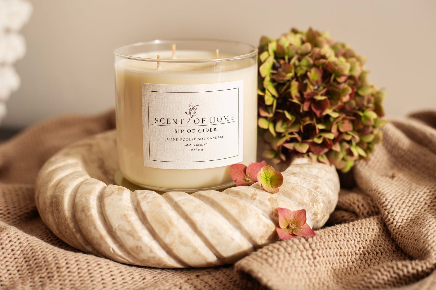 Scent of Home Sip of Cider candle surrounded by cozy textures, hydrangeas, and soft fall tones — warm apple and spice fragrance