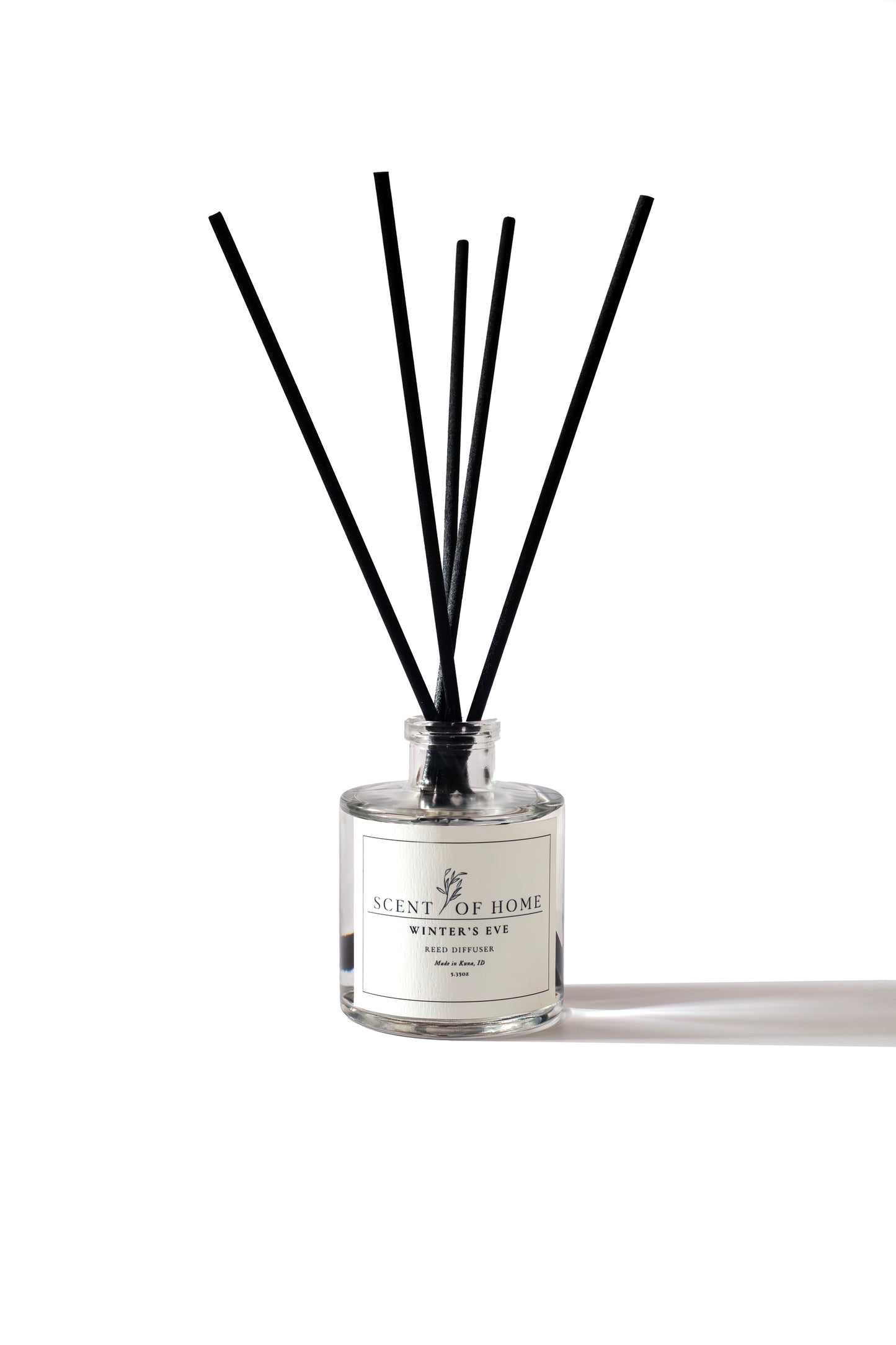 Scent of Home Winter’s Eve reed diffuser on a white background, featuring clear glass bottle, minimalist label, and sleek black diffuser reeds casting a soft shadow.