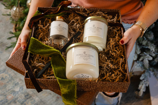 Scent of Home Winter’s Eve holiday gift box with a reed diffuser and two soy candles nestled in crinkle paper, tied with a velvet ribbon and held in both hands.