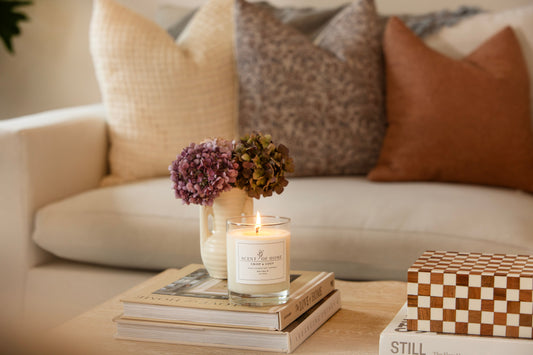 Scent of Home Crisp & Cozy soy candle burning on a coffee table beside hydrangeas and decor books in a warm, inviting living room.