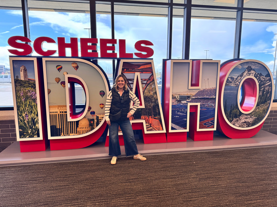 Jessica Cook, founder of Scent of Home, standing in front of the large Scheels Idaho sign after partnering with Scheels to feature her hand-poured soy candles in stores