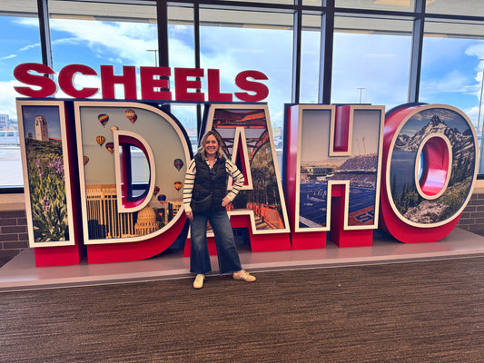Jessica Cook, founder of Scent of Home, standing in front of the large Scheels Idaho sign after partnering with Scheels to feature her hand-poured soy candles in stores