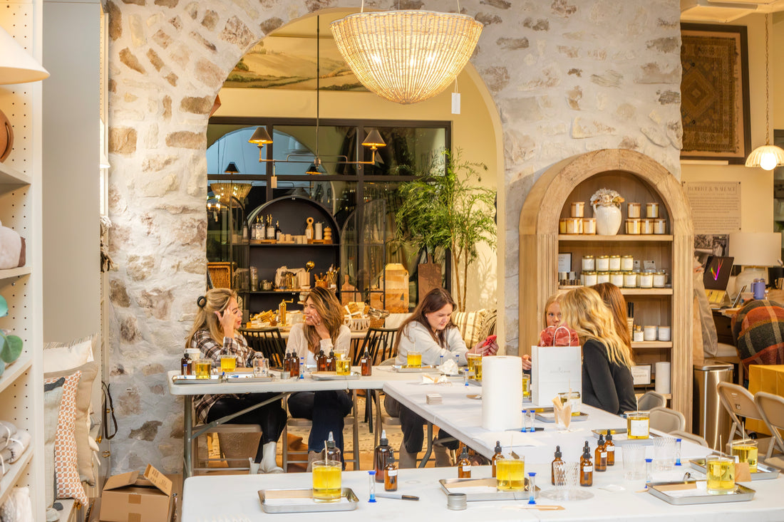 Guests enjoying a Scent of Home candle pouring class at Robert & Wallace, surrounded by candle-making supplies, fragrance oils, and finished candles in a cozy, boutique setting