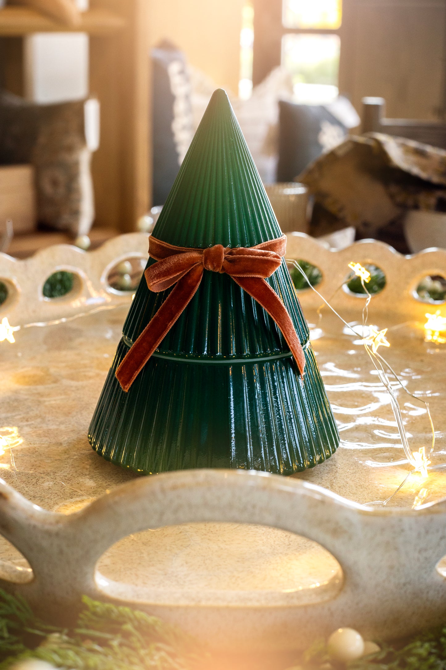 Frosted Juniper Christmas Tree candle with a velvet bow, displayed on a decorative tray with soft holiday lights.