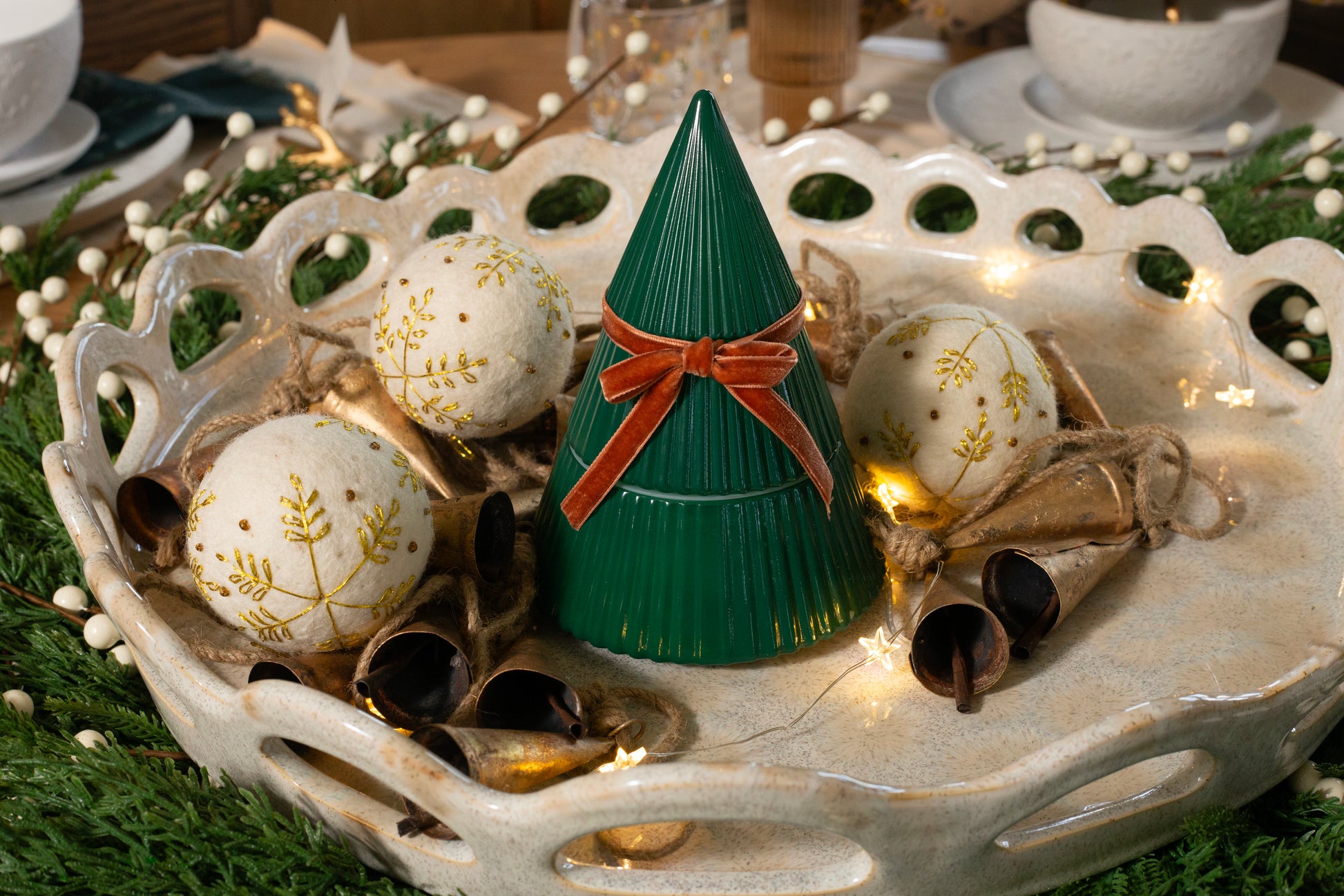 Frosted Juniper Christmas Tree candle in a green tree-shaped vessel with a velvet bow, styled on a festive tray with ornaments and greenery.