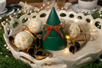 Frosted Juniper Christmas Tree candle in a green tree-shaped vessel with a velvet bow, styled on a festive tray with ornaments and greenery.