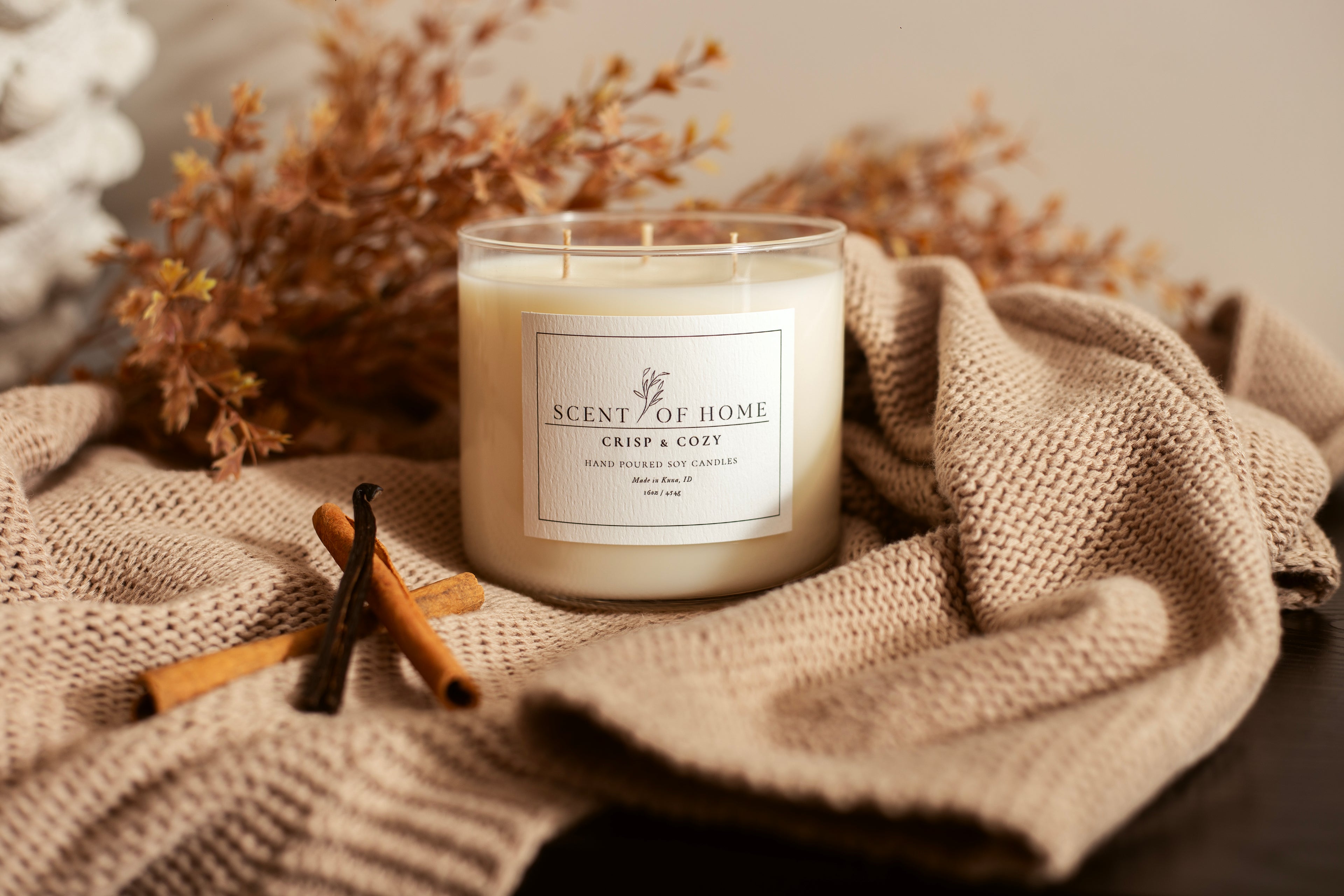 Scent of Home Crisp & Cozy candle surrounded by cinnamon sticks, vanilla bean, and a soft knit blanket — reflecting the warmth and comfort behind every hand-poured candle