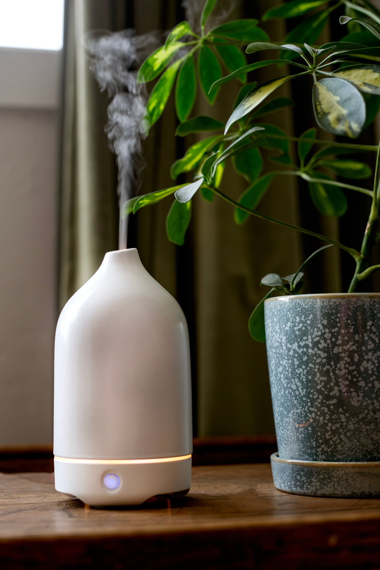 Modern white ceramic essential oil diffuser releasing mist next to a potted plant — clean, non-toxic home fragrance alternative
