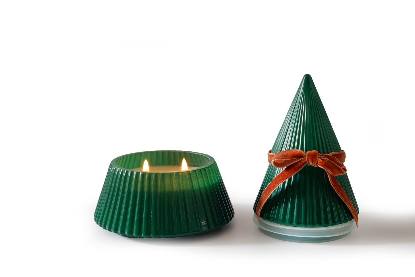 Frosted Juniper Christmas Tree candle with the tree-shaped lid removed, showing the lit candle beside the closed green vessel with a velvet bow, on a white background.