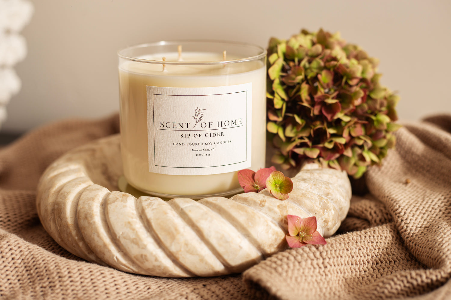 Scent of Home Sip of Cider 16oz 3-wick candle displayed on a marble tray beside hydrangeas and a soft knit blanket — a warm, inviting fall fragrance captured in an elegant soy candle.