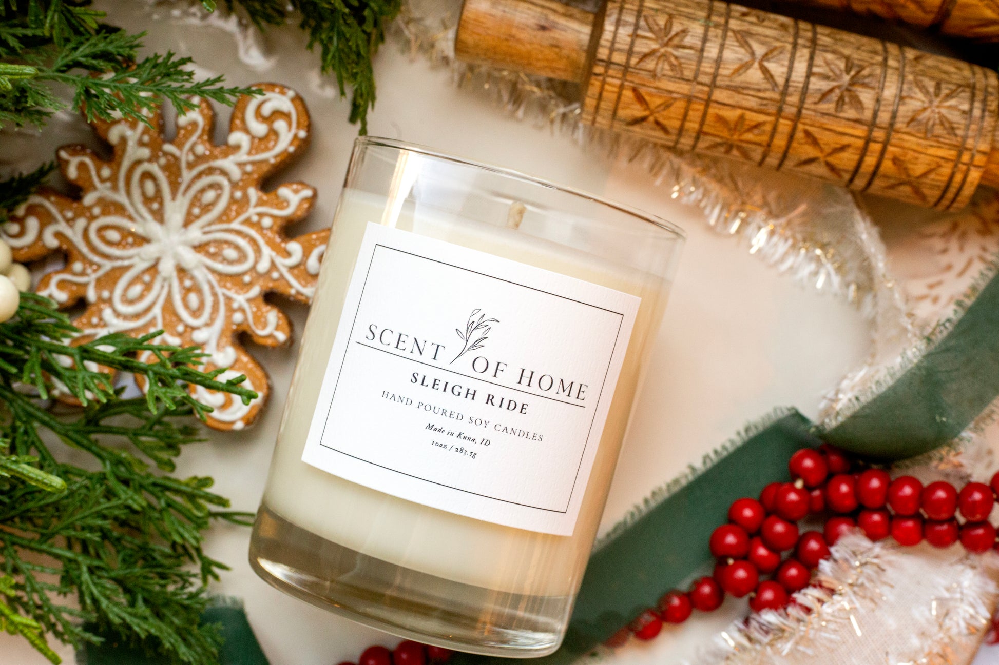 Scent of Home Sleigh Ride soy candle surrounded by holiday greenery, a gingerbread cookie, and red berries.