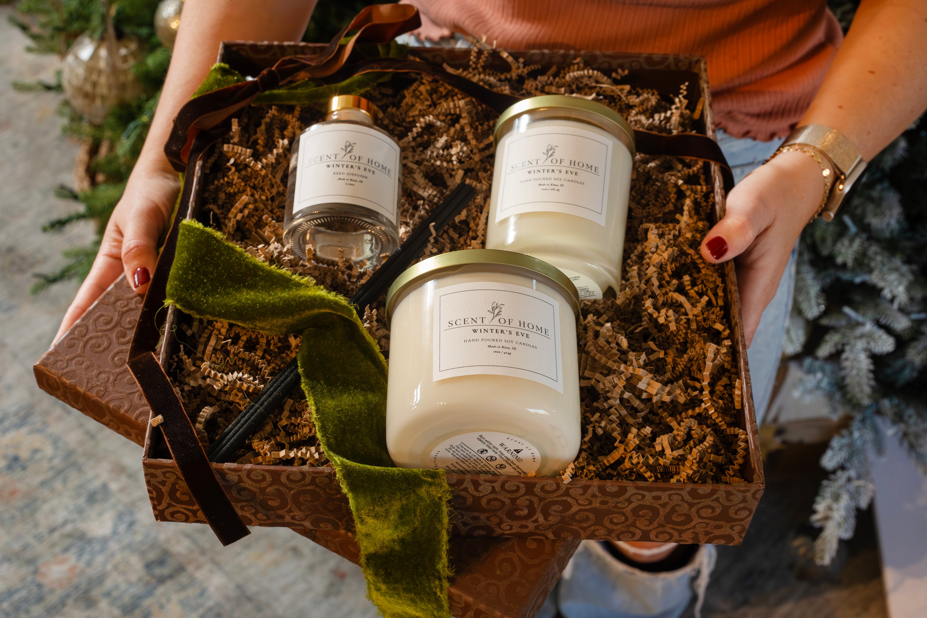 Scent of Home Winter’s Eve holiday gift box with a reed diffuser and two soy candles nestled in crinkle paper, tied with a velvet ribbon and held in both hands.