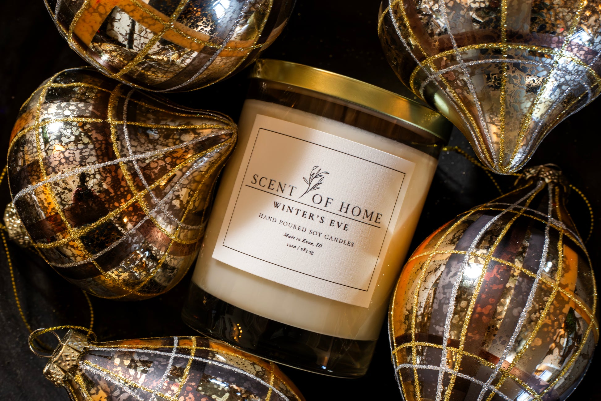 Scent of Home Winter’s Eve candle surrounded by elegant metallic and gold-patterned ornaments, creating a festive and luxurious holiday display.