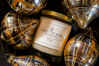 Scent of Home Winter’s Eve candle surrounded by elegant metallic and gold-patterned ornaments, creating a festive and luxurious holiday display.