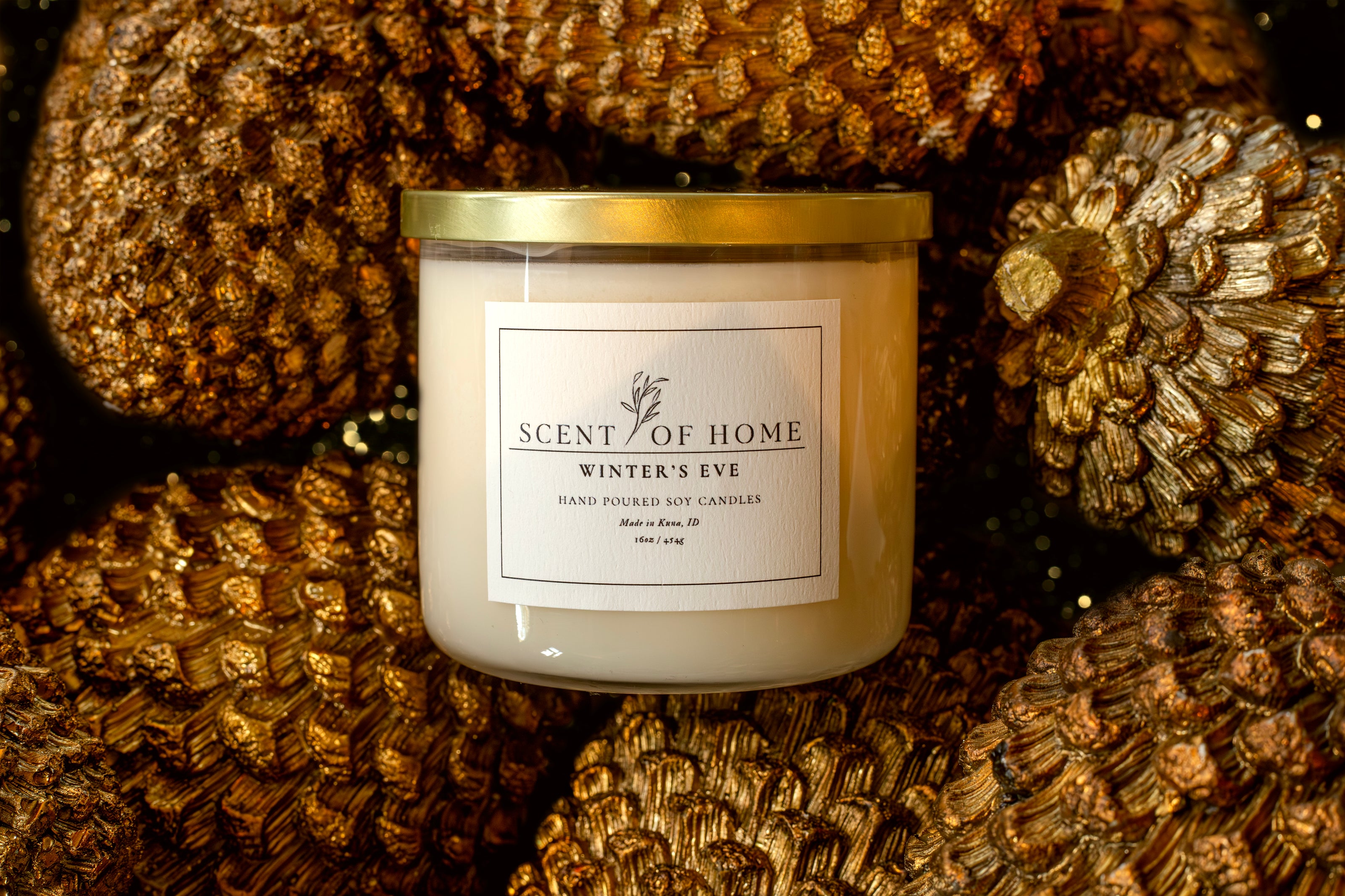 Scent of Home Winter’s Eve candle surrounded by golden pinecones, creating a warm, luxurious holiday scene with rich metallic texture and soft candlelight reflection.